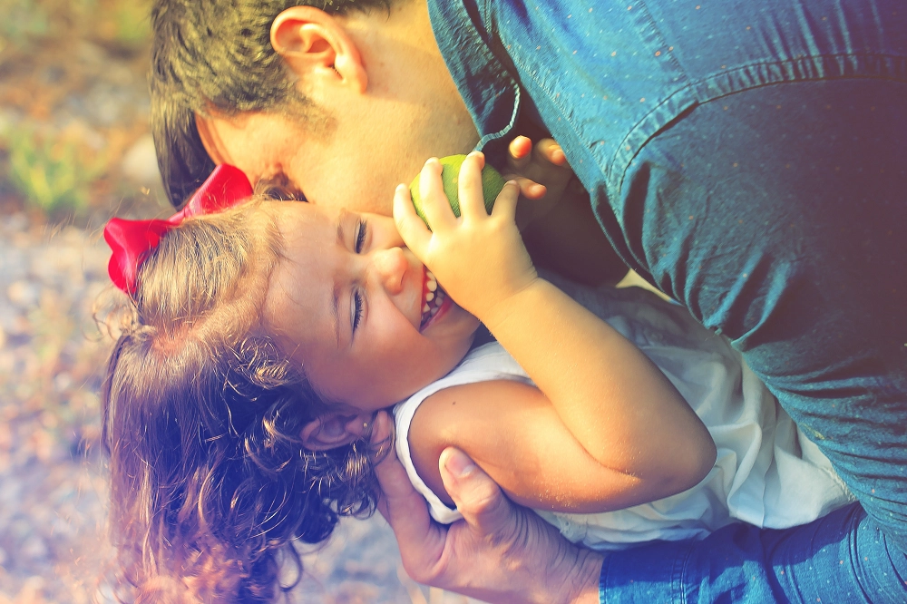 Father hugging and laughing with his young daughter who is smiling and holding an apple