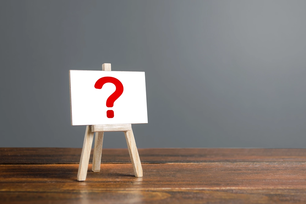 Small easel displaying a white card with a large red question mark on a wooden table