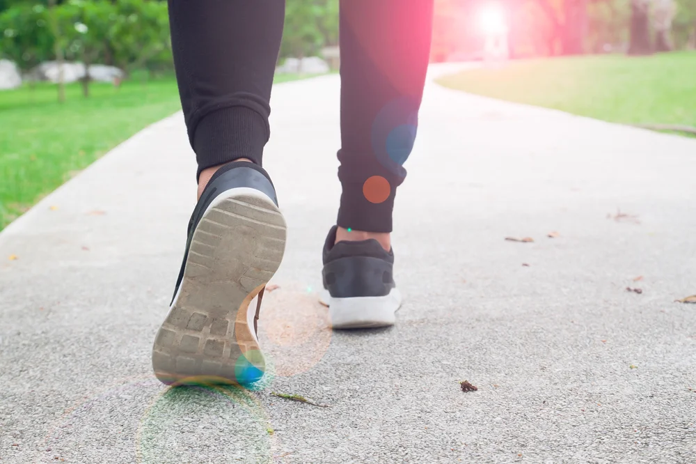 Close-up of a person walking on a paved path in a park with sunlight in the background