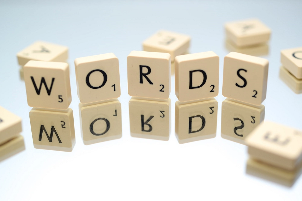 Scrabble tiles spelling the word “WORDS” with their reflection visible on a shiny surface