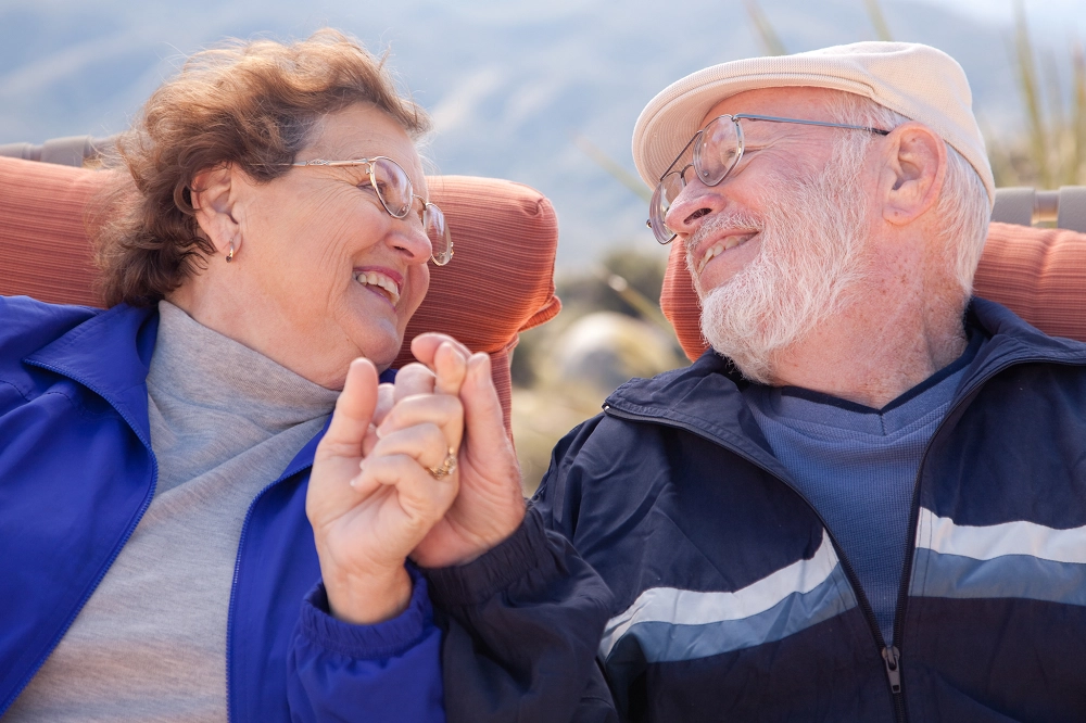 Smiling elderly couple sitting outdoors, holding hands and looking lovingly at each other