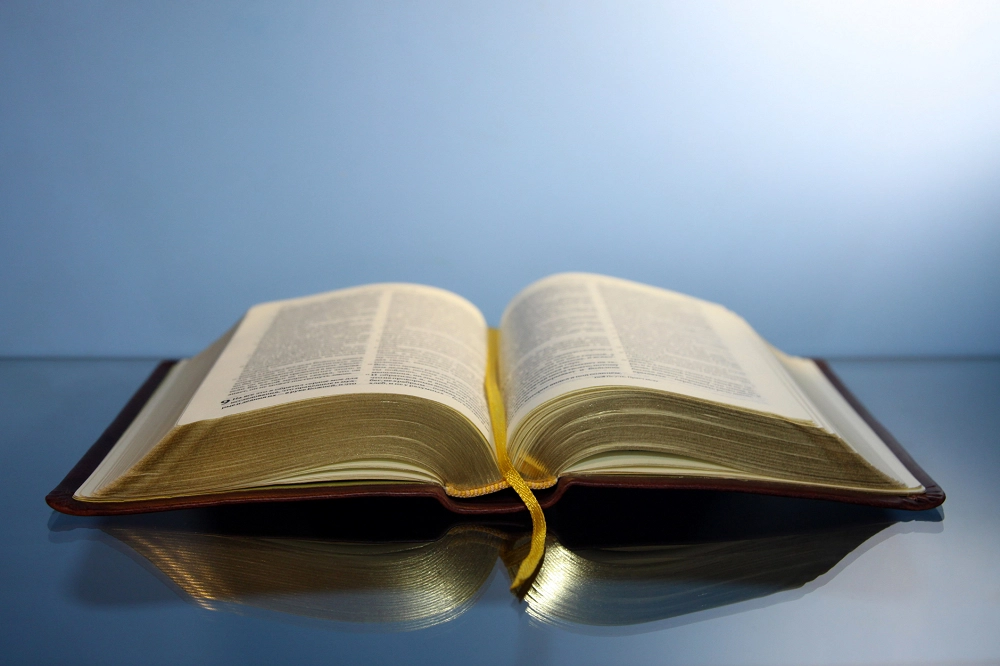 Open Bible with yellow ribbon bookmark on reflective surface against a soft blue background