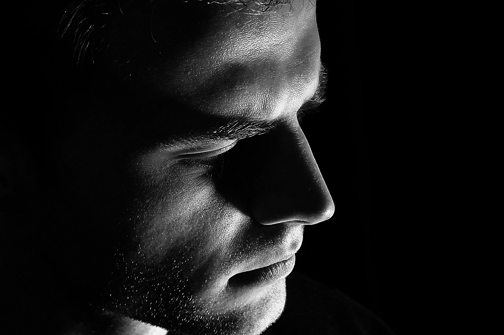 Close-up black and white profile of a man’s face, expressing deep thought or sadness