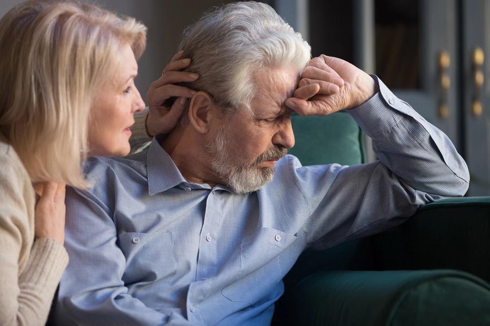 Older woman comforting distressed older man sitting on a couch, showing emotional support and care