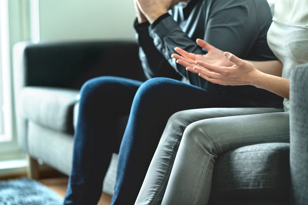 Close-up of people sitting on a couch during a counseling session, with one person gesturing while talking