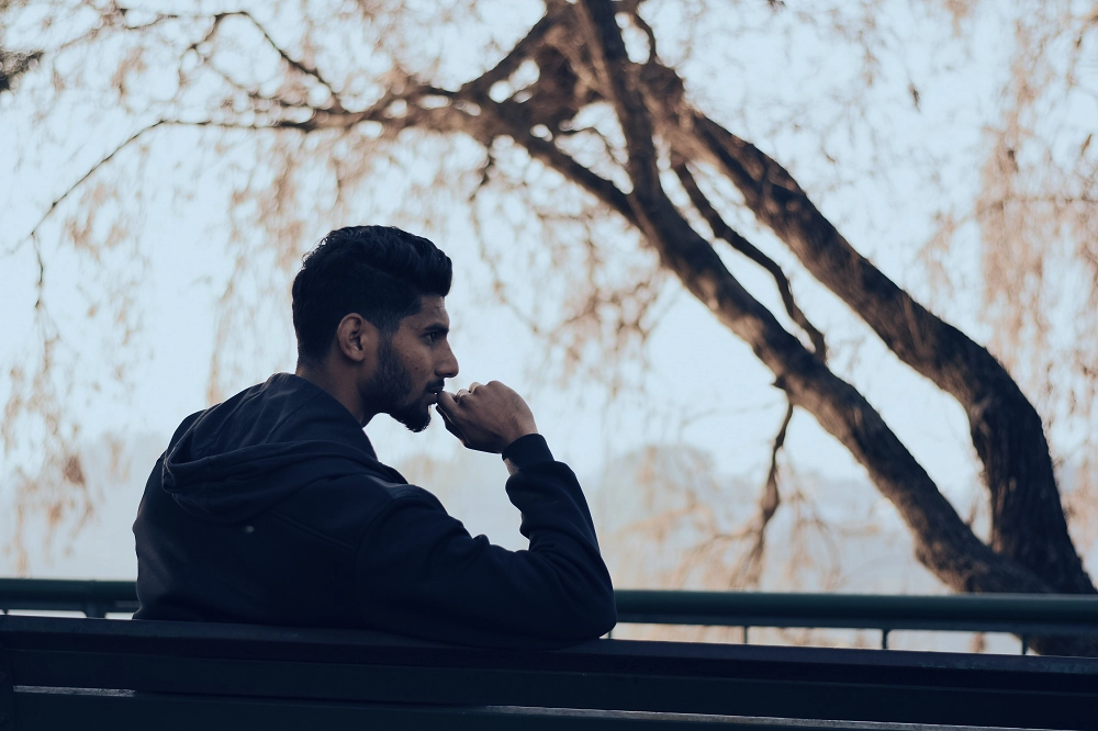 Man sitting alone outdoors, leaning on hand and appearing deep in thought or contemplation