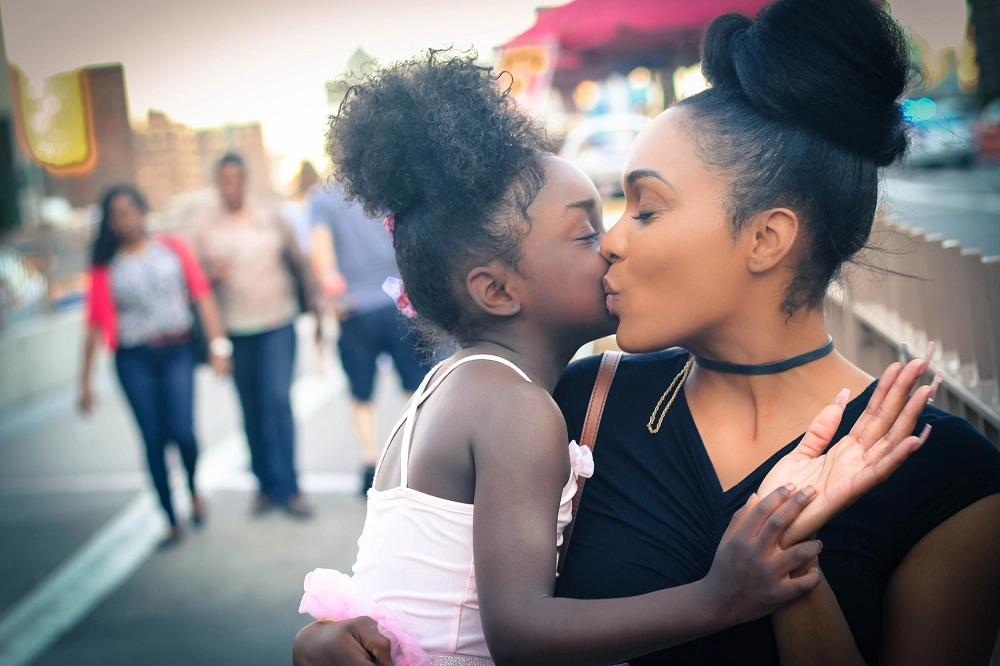 Mother and daughter sharing a loving kiss while standing together on a city sidewalk