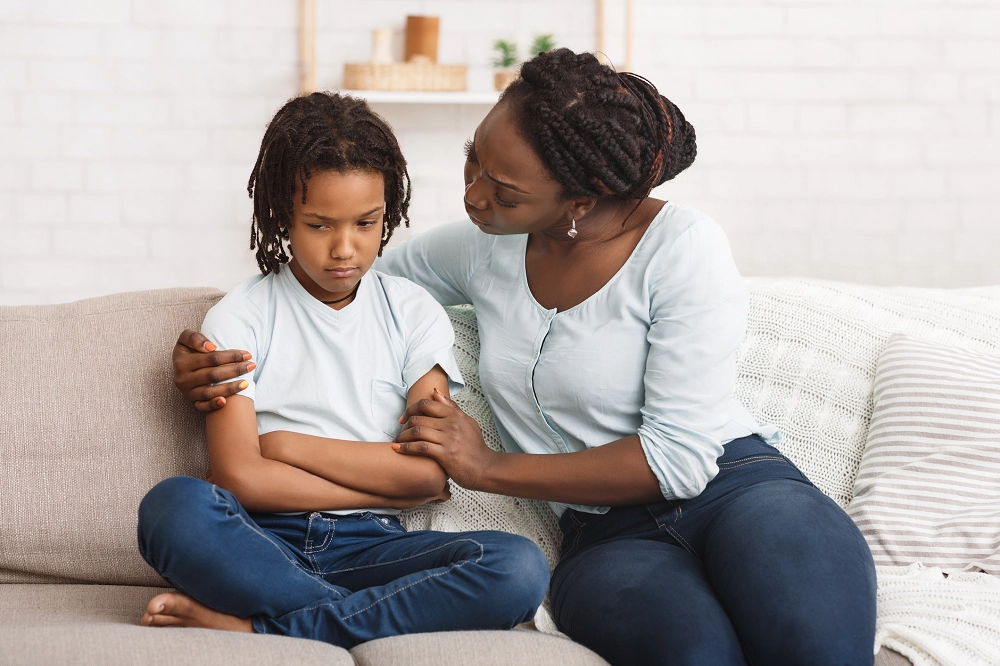 Mother comforting her upset child while sitting together on a couch