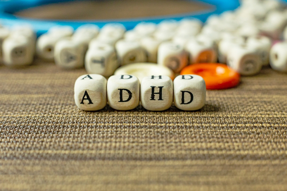 Wooden letter blocks spelling “ADHD” on a table with scattered pieces in the background