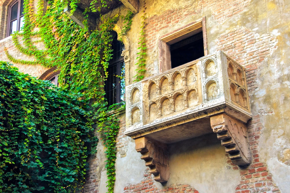 Historic stone balcony covered in ivy on an old brick building, symbolizing romance and timeless beauty