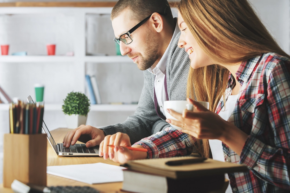 Smiling man and woman working together at a desk with a laptop and coffee cup