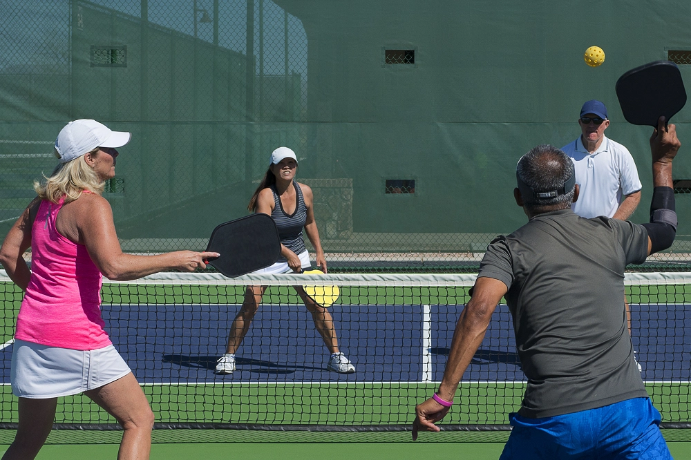 Two men and two women playing doubles pickleball on an outdoor court